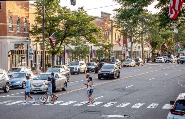 People on a crosswalk with retail shops and cars in the background